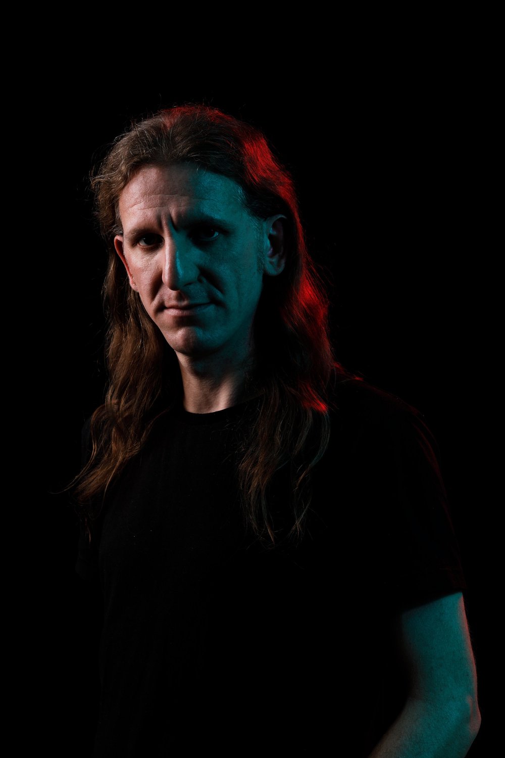 Jonas, Bass, lange Haare, rot und cyan beleuchtet.
